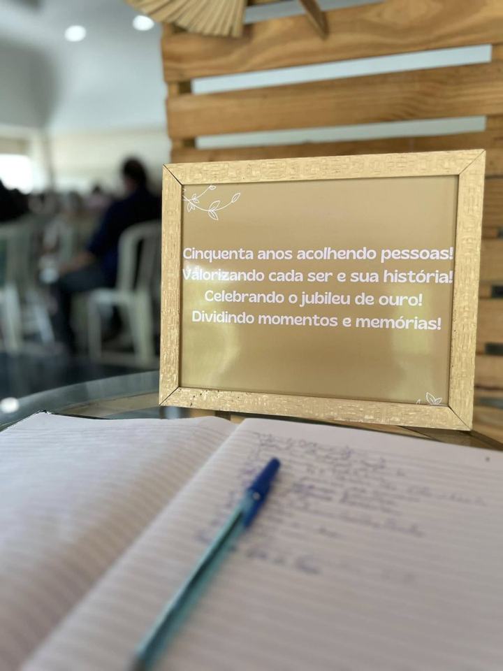 Placa dourada com a frase Cinquenta anos acolhendo pessoas, honrando cada ser e sua história, ao lado do livro de assinaturas